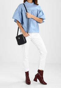 Camicia azzurra a maniche corte con dettagli a ruches, pantaloni bianchi dritti, stivaletti lucidi bordeaux alla caviglia e una piccola borsa a tracolla nera.