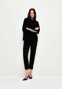 Maglione nero con scollo a cappuccio e dettagli a righe sulle maniche, abbinato a pantaloni neri cropped e décolleté neri con cinturino.