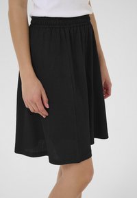 Jupe noire texturée avec une taille élastique, de conception longueur genou, et une finition lisse, présentée sur un fond neutre.