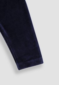 Navyblauwe fluwelen broekspijp met een gladde textuur, een lichte glans en net gestikte naden. De zoom is recht en afgewerkt.