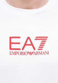 Λευκό T-shirt με κόκκινο λογότυπο "EA7 Emporio Armani" τυπωμένο στο στήθος, με ένα στιλιζαρισμένο ριγωτό νούμερο 7.