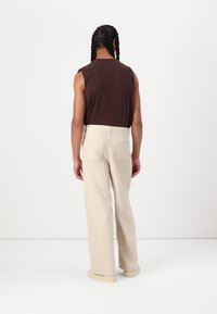 Brown sleeveless top paired with light beige, wide-leg trousers featuring two back pockets. The fabric appears soft with a smooth texture.