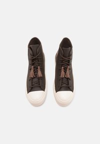 Hnědé vysoké tenisky s koženým svrškem, kontrastní bílou gumovou špičkou a detailem třásní na tkaničkách. Akcenty texturovaného bočního panelu.