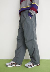 Grå träningsbyxor med elastisk midja, featuring sidofickor och en liten logotyp. Kombination med vita och röda sneakers.