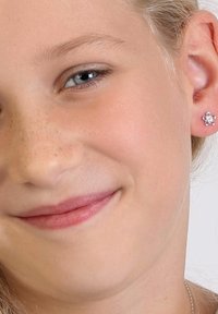 Silberner blumenförmiger Steckerohrring mit kleinen klaren Steinen, getragen von einem jungen Mädchen. Zarte, glatte Haut mit leichten Sommersprossen und einem natürlichen Lächeln.