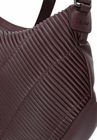 Burgunderfarbene Leder-Schultertasche mit vertikal geripptem Textur, kontrastierenden Nähten und abnehmbarem Schulterriemen. Markenlabel ist auf dem Metallrand sichtbar.