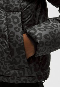 Jachetă puffer neagră cu un model de leopard gri. Are un buzunar pe piept, manșete elastice și un material texturat.