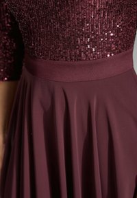 Bordeaux kjole med et besat bodice og en glat, flydende nederdel med folder. Livrem i matchende stof. Elegant teksturkombination.