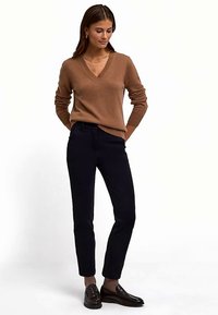 Pull à col en V à manches longues de couleur marron clair, assorti à un pantalon slim foncé. Le pull présente des poignets côtelés, une texture lisse et une coupe décontractée.