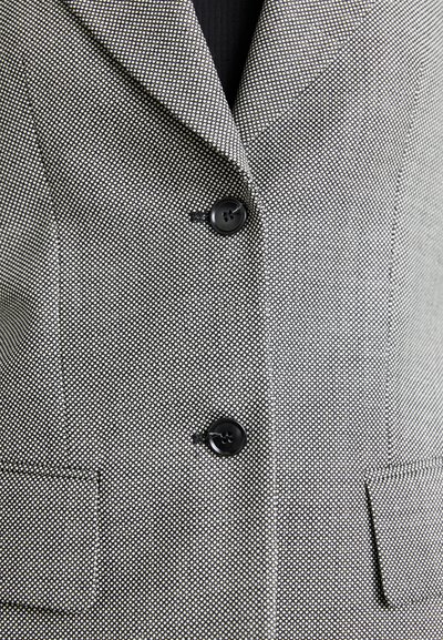 Pukinetta takki, jossa on teksturoitu kangas ja mustavalkoinen pilkku-kuvio. Kaksi mustaa nappia ja kaksi etutaskua. Malli on säädetty istuvuudeltaan.