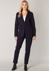 Marineblauwe dameskostuum met een slim-fit blazer en op maat gemaakte broek, gemaakt van een soepele stof. Voorzien van een enkele knoopsluiting en twee zakken.