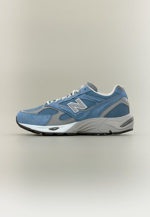 Μπλε και γκρι αθλητικό παπούτσι New Balance με λευκά κορδόνια, μαξιλαρωμένη σόλα και επάνω μέρος από δίχτυ και σουέτ, εμφανίζεται σε πλευρικό προφίλ σε ουδέτερο φόντο.