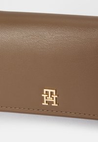 Ruskea nahkalompakko, jossa on teksturoitu pinta, kultasävyinen logo ja siisti ommel reunoilla.