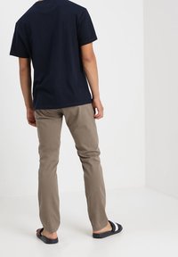 Granatowy bawełniany t-shirt, jasnobeżowe spodnie oraz czarno-szare sandały; widok od tyłu z widocznymi szwami i fakturą materiału.