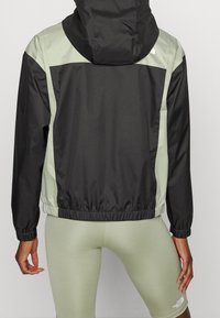 Lekka kurtka z czarno-jasnozielonym wzorem, elastycznymi mankietami i luźnym krojem. Miękka, gładka tekstura.