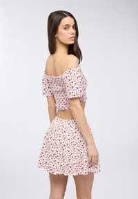 Top corto bianco off-the-shoulder e gonna coordinata con motivo floreale rosso, vita arricciata e orlo a volant. Tessuto dalla texture liscia.