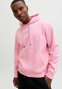 Sweat à capuche rose avec une poche avant et des cordons de serrage. Présente un texte logo blanc "JACK & JONES" sur la poitrine, associé à un pantalon foncé.