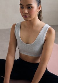 Gray cropped tank top made of soft fabric with a scoop neckline. Worn with black bottoms, showcasing a smooth, fitted silhouette.