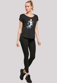 Svart t-skjorte med uformell hals, prydet med en fargerik grafikk av en karakter og snøflak, kombinert med svarte leggings og joggesko.