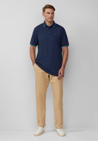 Marineblaues Poloshirt mit Türkisakzenten, Knopfleiste, kombiniert mit beigen Hosen und weißen Turnschuhen, bietet eine lockere Passform und einen glatten Stoff.