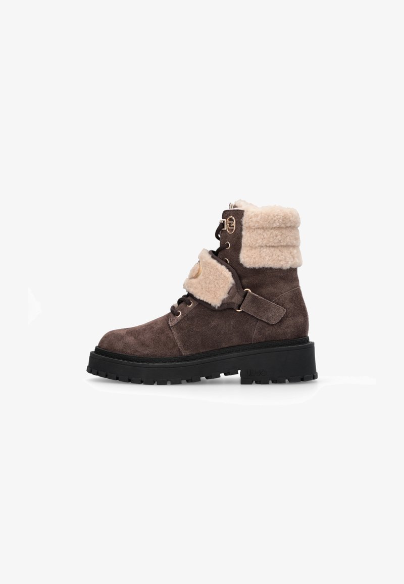 Braune Wildleder-Ankle-Boots mit einem cremefarbigen Kunstfellkragen, Schnürung und Riemenakzenten, einer dicken schwarzer Gummisohle und einem abgerundeten Zehendesign.