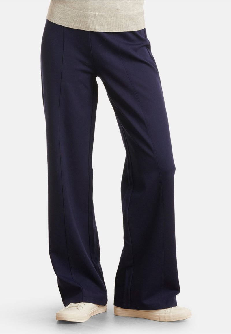 Navy wide-leg pants made from soft fabric with a smooth texture, featuring front seams and paired with light-colored canvas shoes.