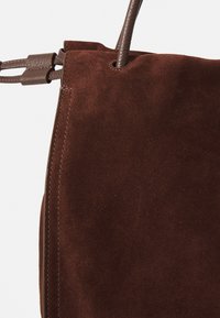 Borsa a tracolla in suede marrone con una texture morbida, sottile tracolla in pelle marrone e dettagli di cucitura lungo i bordi.