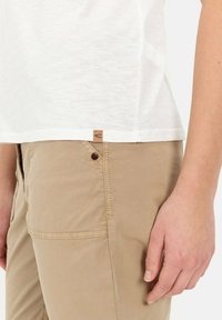 Witte t-shirt met korte mouwen en een textuurafwerking, gecombineerd met lichtbeige broek met een knoopsluiting en een zichtbare zijzak.