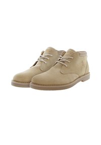 Botas chukka de ante beige con punta redonda, cordones de color crema y suela de goma marrón. Logo grabado en el lateral para dar un toque de detalle.