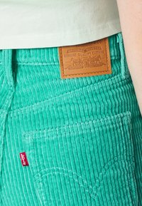 Pantalones de pana turquesa con textura acanalada, que cuentan con una etiqueta de cuero marrón y una etiqueta roja de Levi's en el bolsillo trasero.