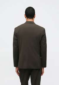 Καφέ σακ�άκι προσαρμοσμένο με αναδιπλούμενους γιακάδες, μεμονωμένο πίσω σκίσιμο και κουμπωμένα μανίκια. Λείο ύφασμα με δομημένη εφαρμογή.