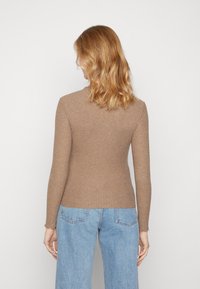 Top marrone a maniche lunghe con coste, dal taglio aderente. Presenta un collo a giro e rifiniture sofisticate ai bordi dei polsini. Abbinato a jeans blu chiaro.