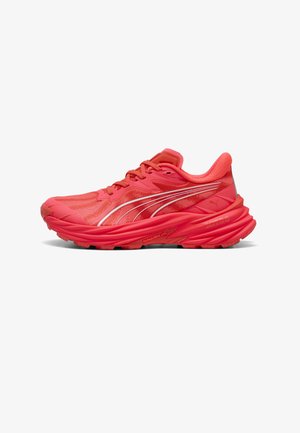 Chaussure de sport rouge vif avec une semelle épaisse, un col rembourré et des bandes blanches incurvées du logo sur le côté, vue de l'extérieur.