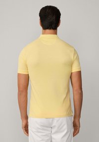 Polo tričko v měkké žluté bavlně. Krátké rukávy, klasický límeček a rovný lem s bočními rozparky. Minimalistický design bez viditelných log.