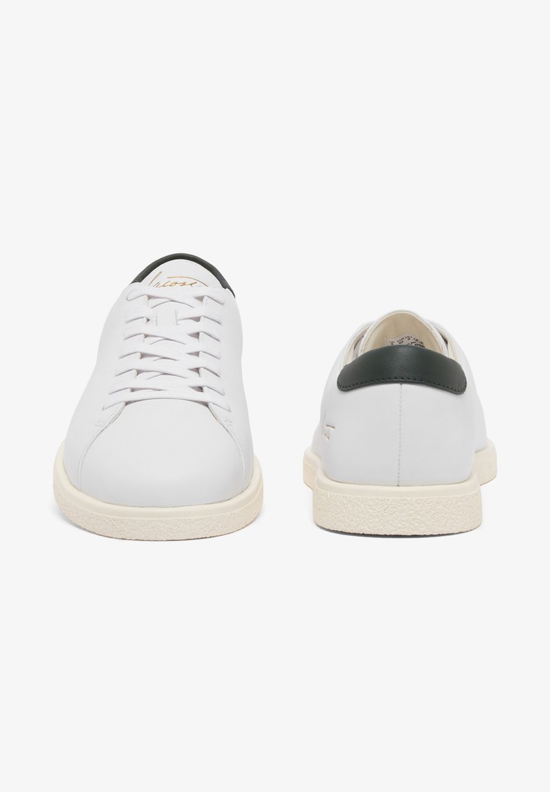 Coppia di scarpe da ginnastica basse bianche con suole color crema, dettagli neri sul tallone e lacci, viste frontali e posteriori su sfondo bianco.