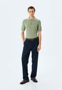 Grön ribbad kortärmad polo skjorta med tre knappar, kombinerad med mörkblå byxor och mörkbruna slip-on skor.