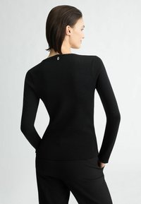 Maglietta nera a maniche lunghe con texture a coste, dotata di scollatura rotonda e un piccolo dettaglio con logo sulla nuca. Abbinata a pantaloni neri.