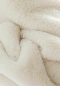 Krämfärgad plyschfilt med en mjuk, texturerad yta, som har ett tjockt, fluffigt utseende och milda veck.