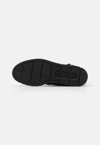 Suela de zapato de goma negra con patrones de relieve texturizados, que presenta un logotipo en forma ovalada. Perfil plano, diseñado para estabilidad y agarre.