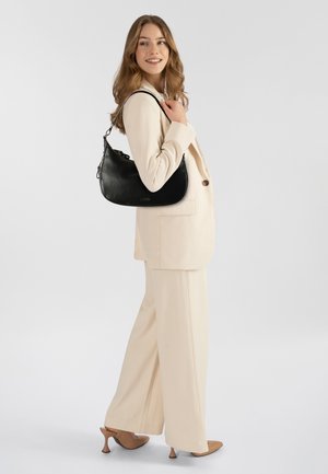 Zwarte leren schoudertas met een gladde textuur, gebogen ontwerp en zilveren details, gedragen over de schouder bij een lichtgekleurde jurk.