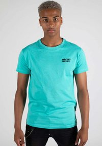 Türkises Baumwoll-T-Shirt mit rundem Ausschnitt, kurzen Ärmeln und einem schwarzen "WRONG FRIENDS"-Logo auf der linken Brust. Glatte Textur.