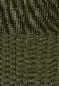 Tessuto verde testurizzato con un motivo a costine nella parte superiore e una sezione liscia sottostante, che mostra un design monocromatico.