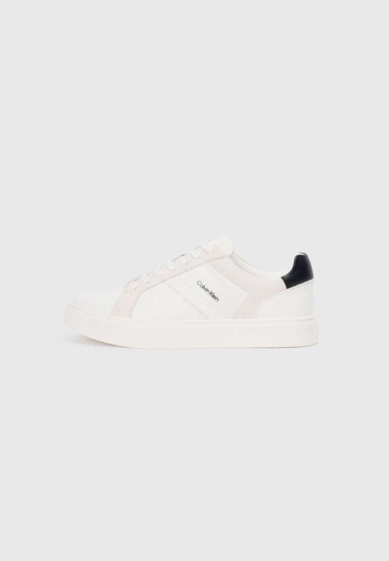 Zapatillas blancas con acentos en rosa claro y negro, que presentan paneles de cuero suave y gamuza, punta redonda y suela plana de goma.