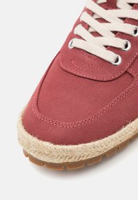 Baskets en toile rouge avec un contour en jute beige, bout rond et lacets crème. Présente des œillets en métal et une semelle en caoutchouc texturé.