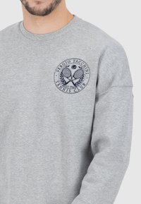 Felpa grigia realizzata in tessuto morbido, con scollatura rotonda e un design del logo con un motivo tennis in blu navy sul petto.