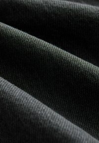Tmavě zelená pletená látka s jemnou texturou, zobrazuje detailní pohled na propletená vlákna a jemné rýhy, zdůrazňující její pružnost a teplo.