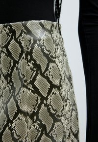 Jupe à motif de serpent avec une finition brillante, dans des tons de vert et noir atténués, présentant une silhouette ajustée et une texture lisse.