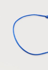 Λεπτό μπλε πλεκτό κορδόνι δεμένο σε θηλιά σε απλό λευκό φόντο.