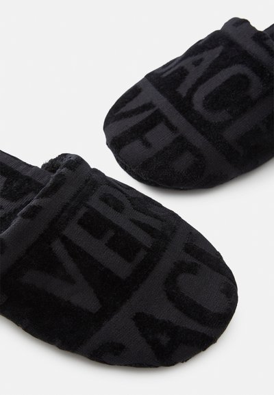Μαύρα πλισέ παντόφλες με μαλακή υφή, που διαθέτουν τολμηρά, υφασμένα γράμματα σε όλη την επιφάνεια. Σχεδίαση κλειστού δαχτύλου με επενδεδυμένη σόλα.