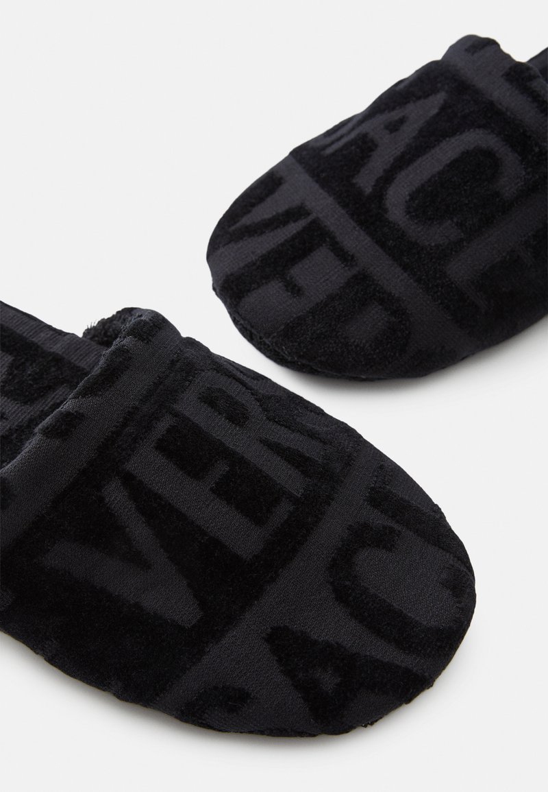 Sorte plyssandaler med en blød tekstur, prydet med dristige, teksturerede bogstaver på stoffet. Design med lukket tå og polstret sål.